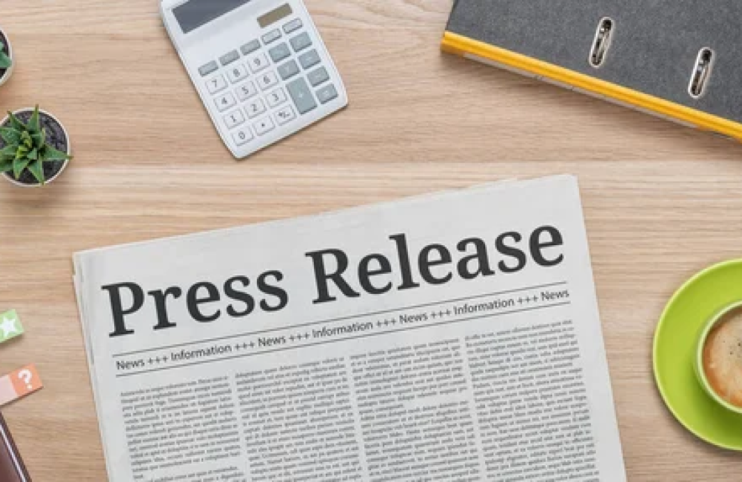 light wood table with a calculator and a newspaper on it that has the headline "Press Release"